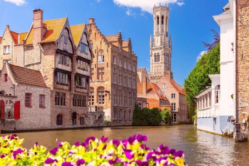 A canal with historic buildings, a tower, and vibrant flowers. 1