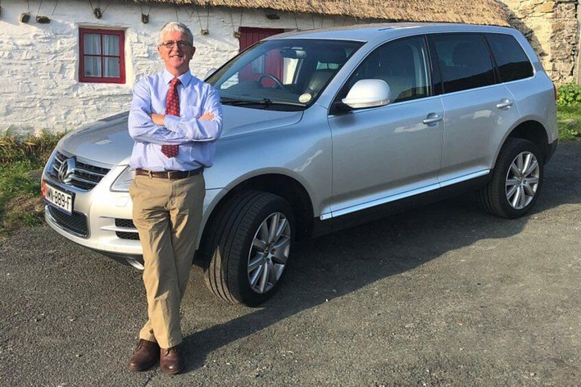 A silver SUV parked in front of a stone building with a red window. 1