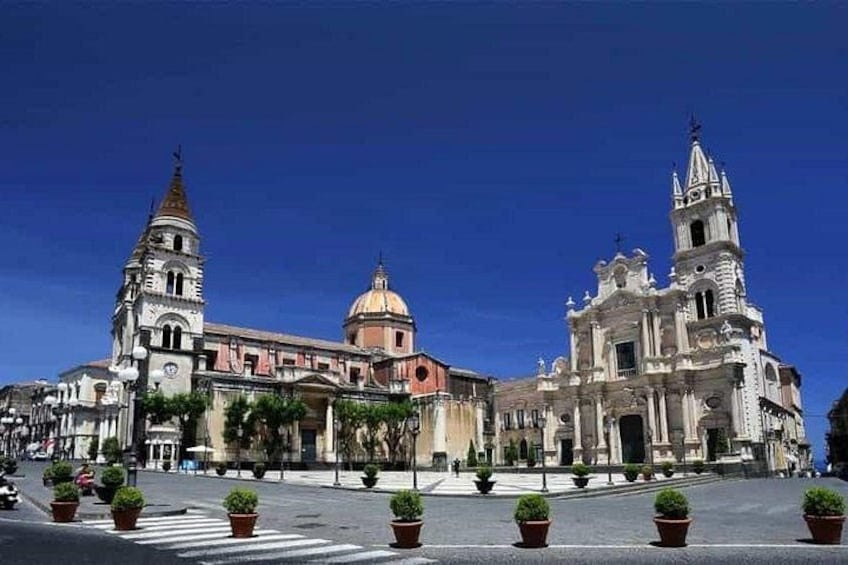 A historic plaza with a prominent church featuring a bell tower and dome, surrounded by potted plants and a crosswalk. 2