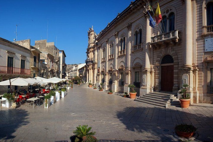 A historic square with buildings, outdoor seating, and flags. 2