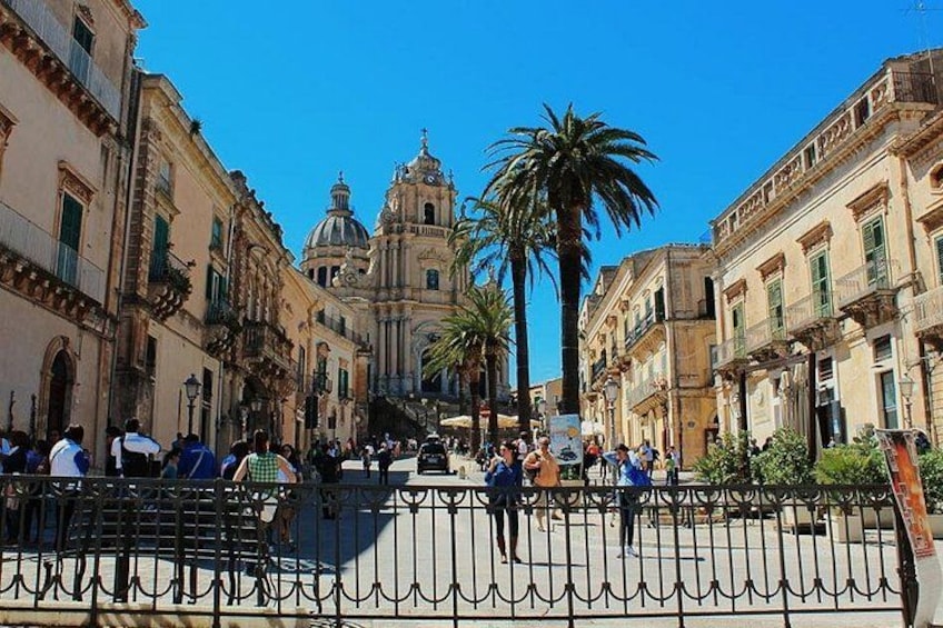 A bustling square with historic buildings, a prominent church, and a palm tree. 1