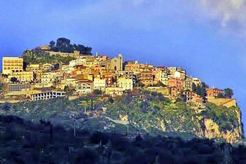 Una cittadina costiera con edifici su una collina, una chiesa in evidenza e un litorale roccioso. 2
