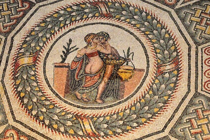 Ein Mosaik mit einer zentralen Figur, die eine Schale hält, umgeben von einem geometrischen Rahmen. 5
