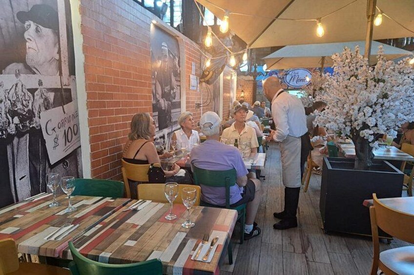 Un ristorante all'aperto con clienti che cenano, un cameriere che serve un tavolo e un cartello che pubblicizza un'offerta speciale. 3