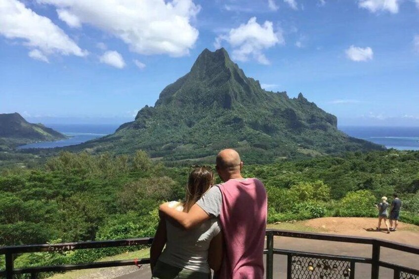 A couple embracing on a scenic overlook with a mountain and ocean in the background. 1