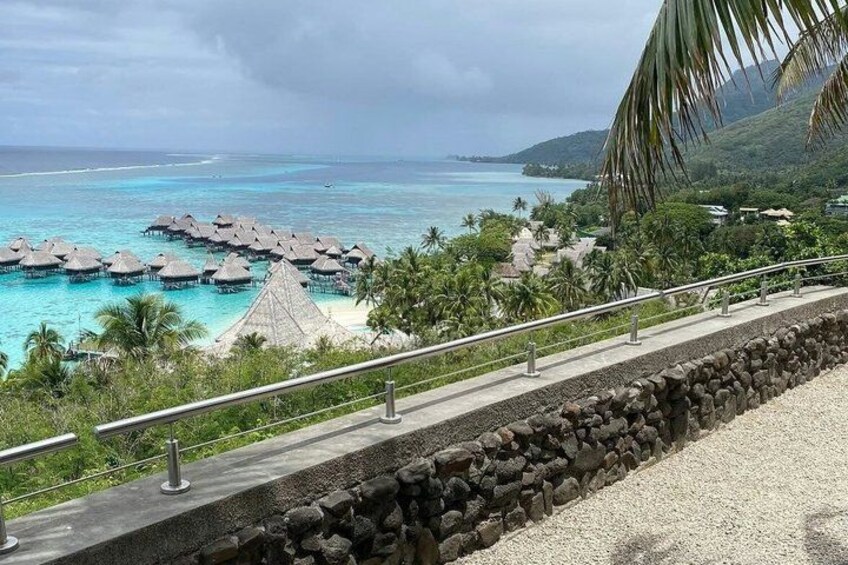 A beach with overwater bungalows, a stone wall, and a palm tree. 3