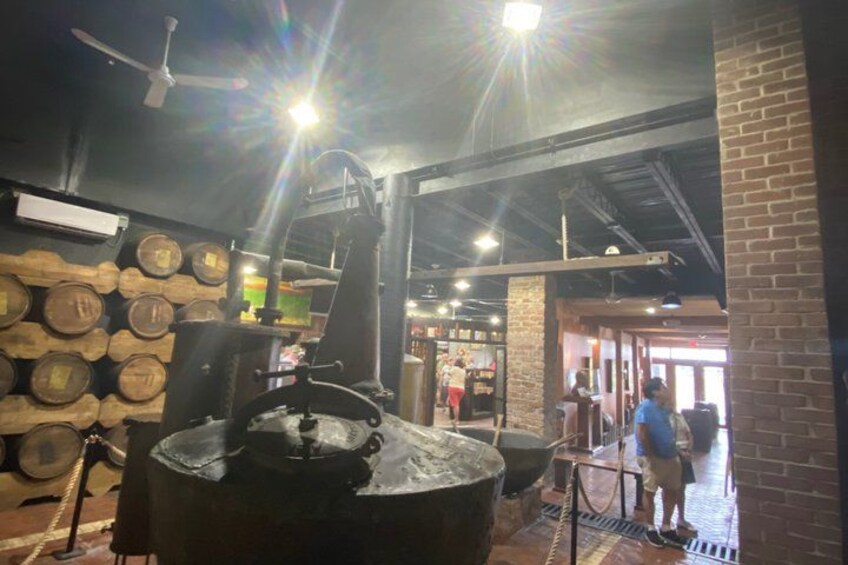 Un interior rústico con una olla de metal grande, barriles de madera y una pared de ladrillo. 4