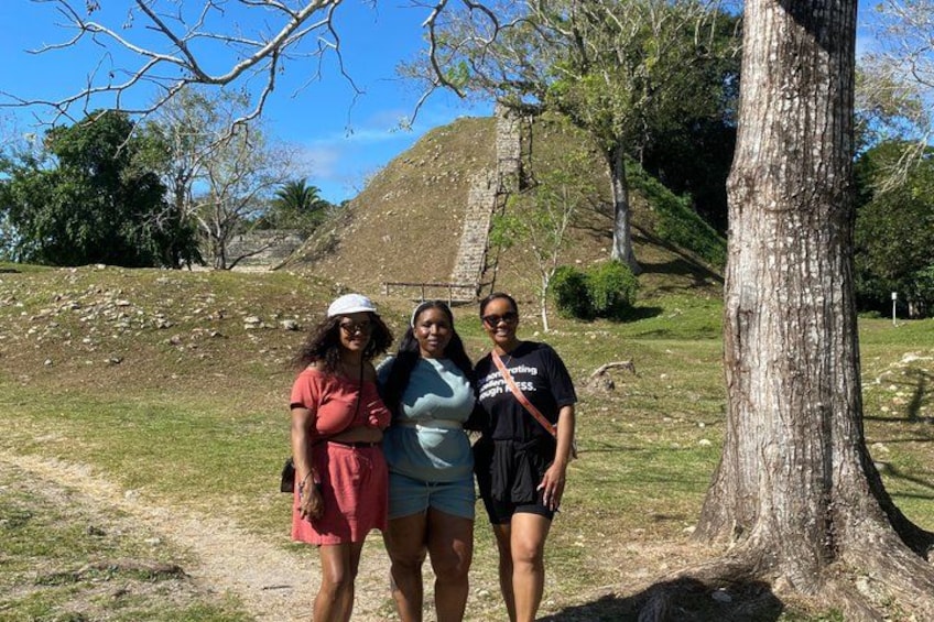 Three people standing near a large tree and a hill in a park. 1