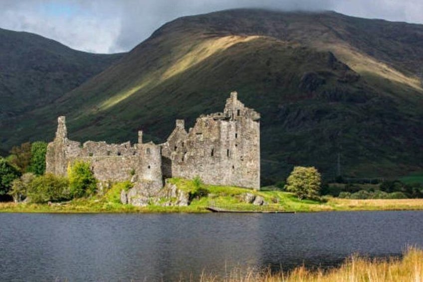A historic stone castle by a lake with a mountainous backdrop. 2
