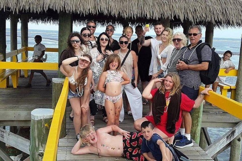 Un grupo de personas en un muelle de madera con techo de paja, contemplando el océano. 5