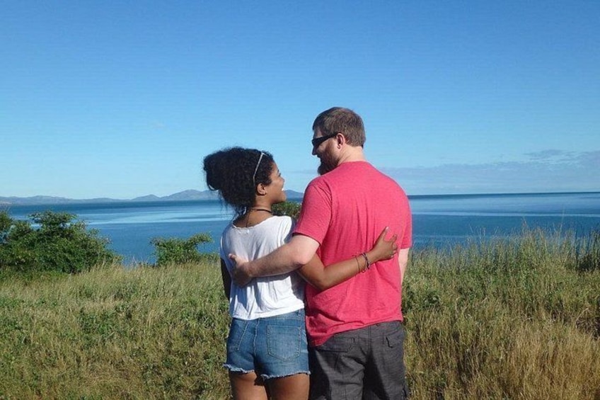 Two people standing on a grassy hill overlooking a body of water with mountains in the distance. 5