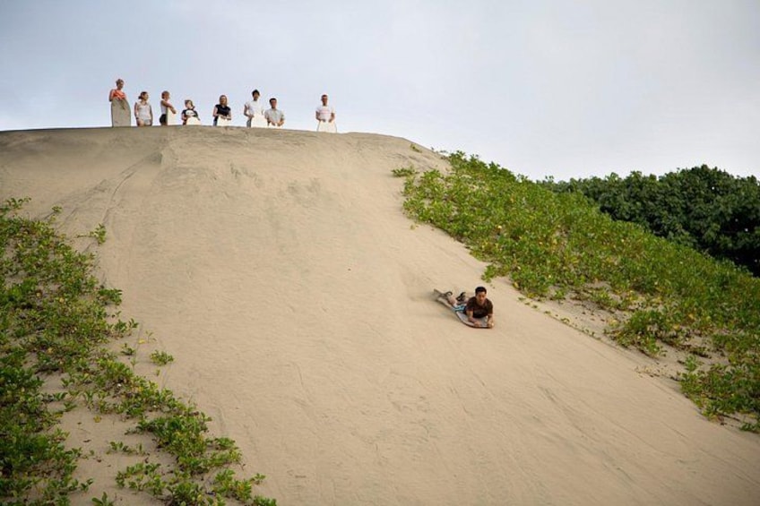 A sandy slope with a person sliding down and others watching. 3