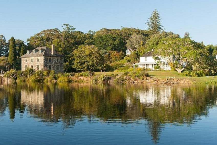 A calm lake with a stone house and a white house on the shore, surrounded by trees and greenery. 1