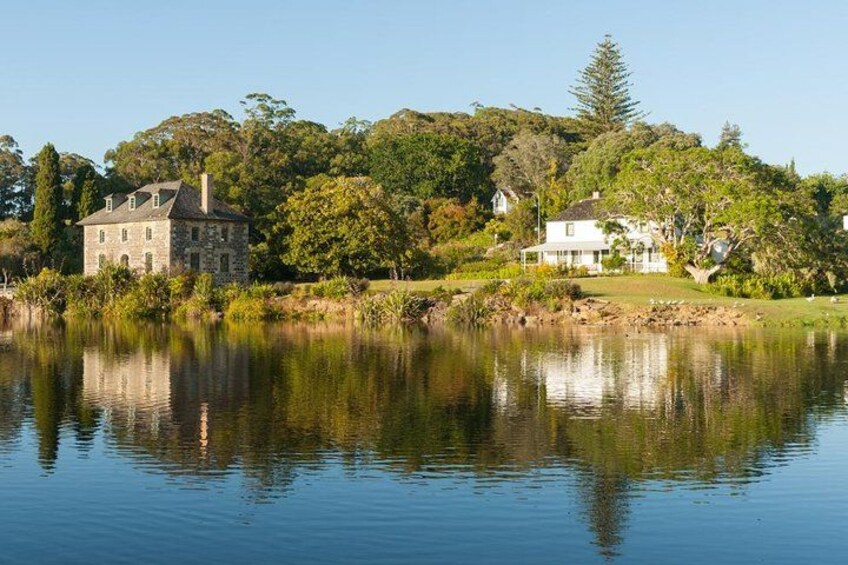 A calm lake with a stone house and a white house on the shore, surrounded by trees and greenery. 1