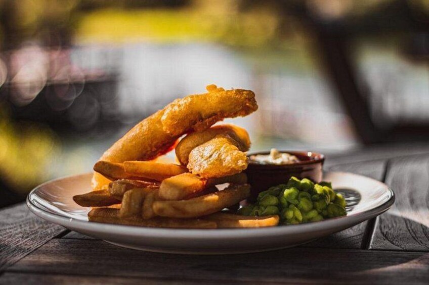 A plate of fish and chips with a side of mushy peas and tartar sauce. 4