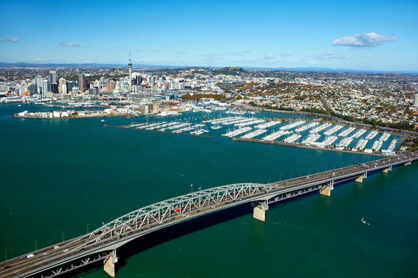 A bridge over a marina with boats, a city skyline, and a clear sky. 2