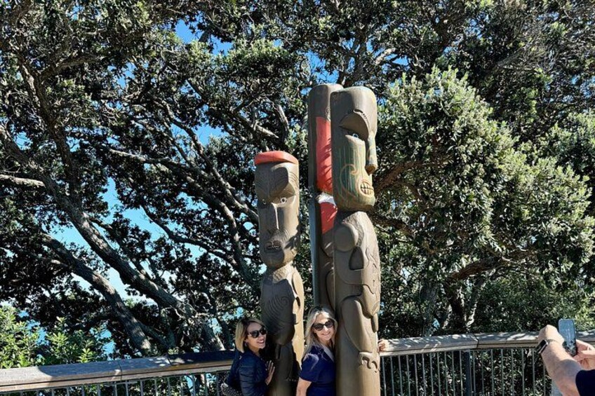 Two totem poles with a railing and trees in the background. 4