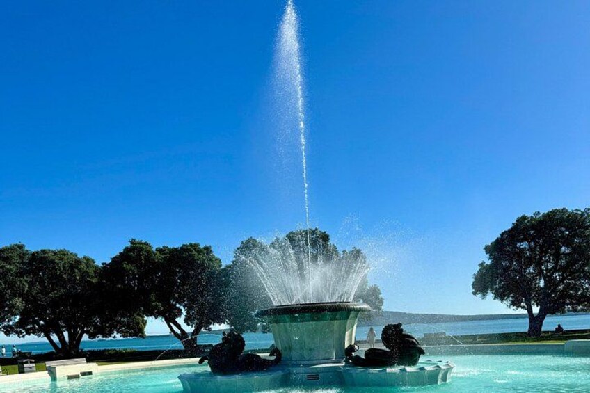 A fountain with water jets, surrounded by trees and a clear blue sky. 2