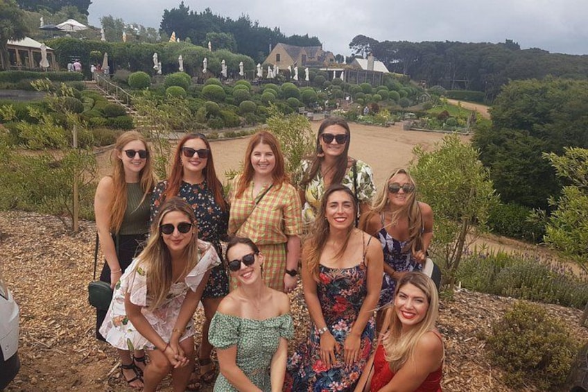 Un groupe de personnes se trouve à l’extérieur, dans un jardin orné de statues, avec un grand bâtiment en arrière-plan. 2