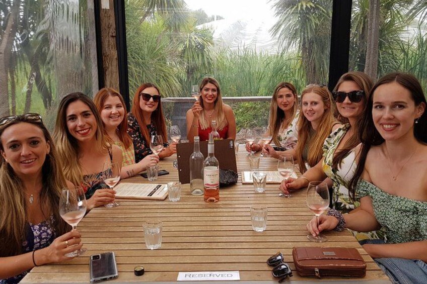 A group of people seated at a wooden table outdoors with a view of greenery. 2