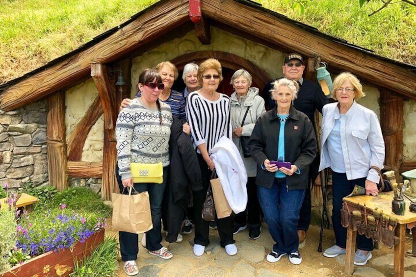 A group of people standing in front of a rustic stone building with a thatched roof. 2