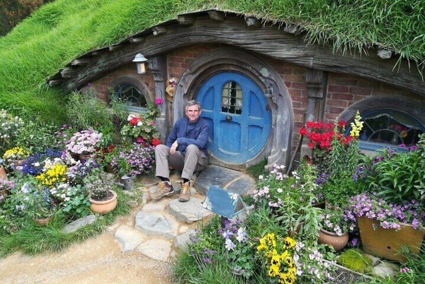A Hobbit-style house with a blue door, surrounded by colorful flowers and greenery. 1