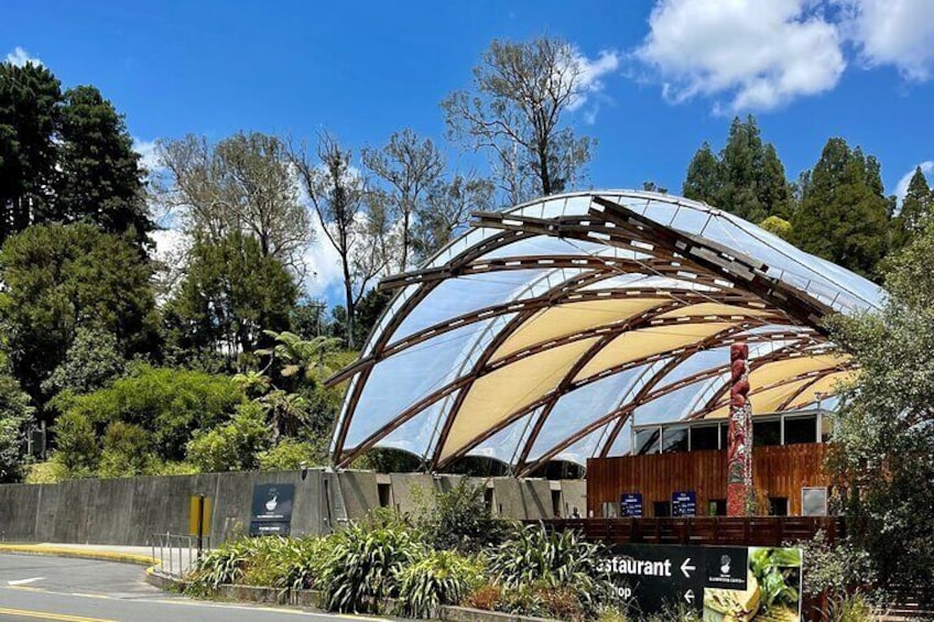 A modern building with a curved glass roof, surrounded by lush greenery and trees. 1