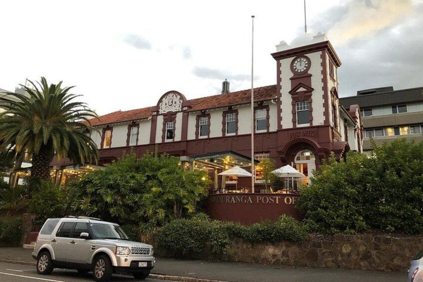 Un edificio histórico con una torre de reloj, palmeras y un automóvil estacionado. 3