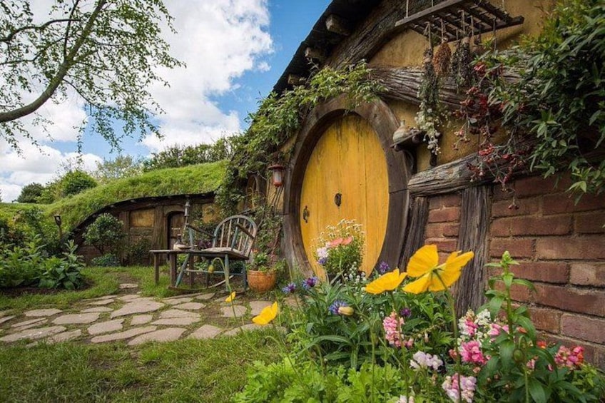 Una casa al estilo Hobbit con una puerta redonda, una silla de madera y un camino de piedra. 1