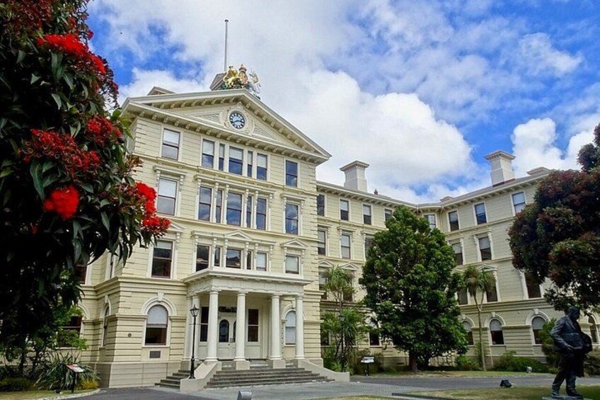 A large, historic building with a clock tower, surrounded by lush greenery and red flowers. 5