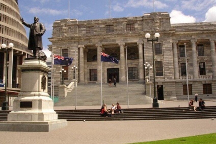 A large building with a statue in front, steps leading up to the entrance, and flags on poles. 3