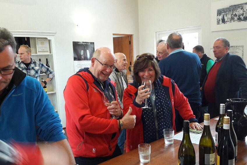 People at a social gathering, some holding glasses, with wine bottles on a table. 1