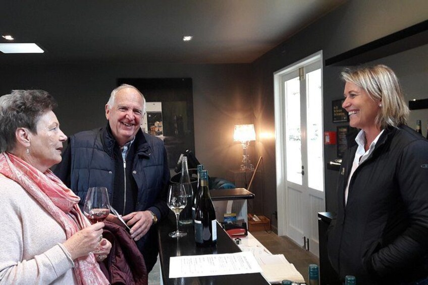 Three people standing at a bar with wine bottles and glasses. 2