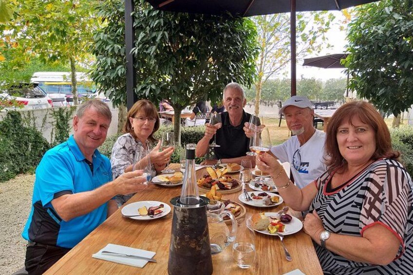 A group of people dining outdoors at a wooden table with food and drinks. 3