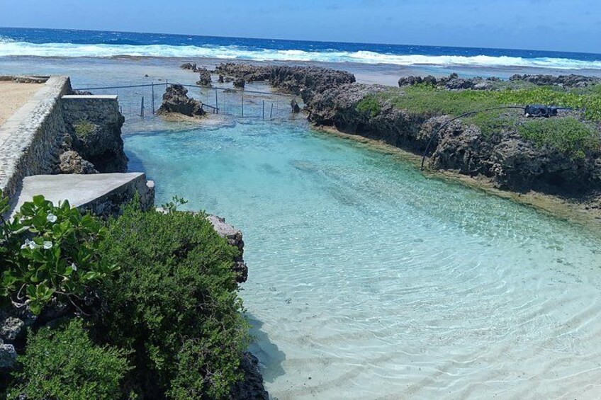 Paisaje costero con aguas turquesas cristalinas, una costa rocosa y un muro de hormigón. 2