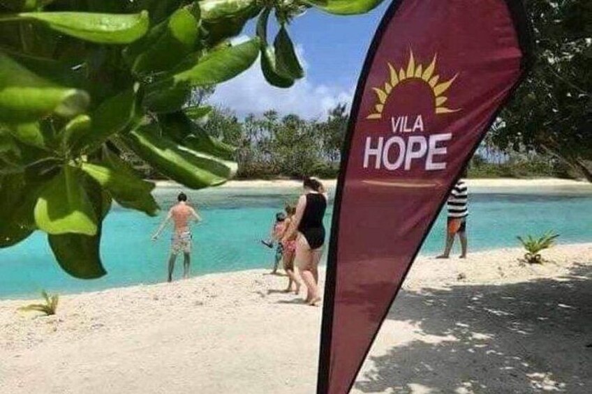 Een strand met mensen die zwemmen en een vlag waarop 'VILA HOPE' staat. 3