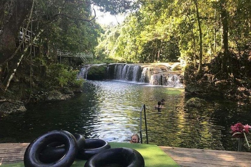 Een waterval, een houten terras en iemand die in een vijver zwemt. 2