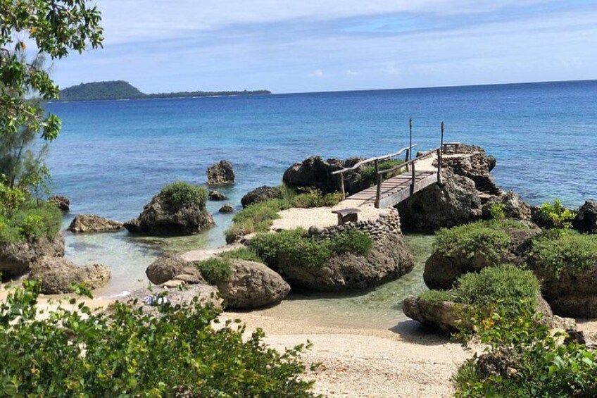 A coastal landscape with large rocks, a wooden walkway, and clear blue water. 2