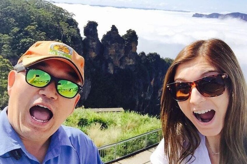 Two people in front of a scenic landscape with rock formations and greenery. 1