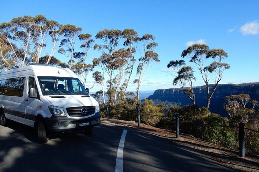 Un fourgon blanc est garé sur une route offrant une vue pittoresque sur des arbres et une chaîne de montagnes en arrière-plan. 2