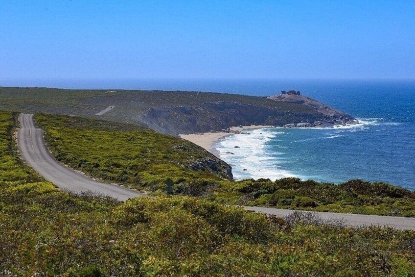 A coastal road curving along a cliffside, overlooking a beach and the ocean. 2