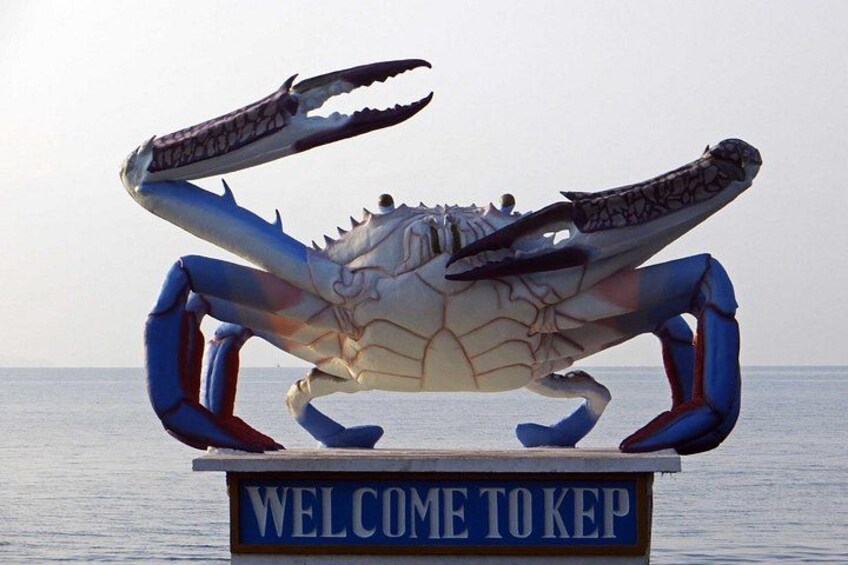 En stor krabbeskulptur med et skilt, der siger 'WELCOME TO KEP', foran et roligt hav. 1