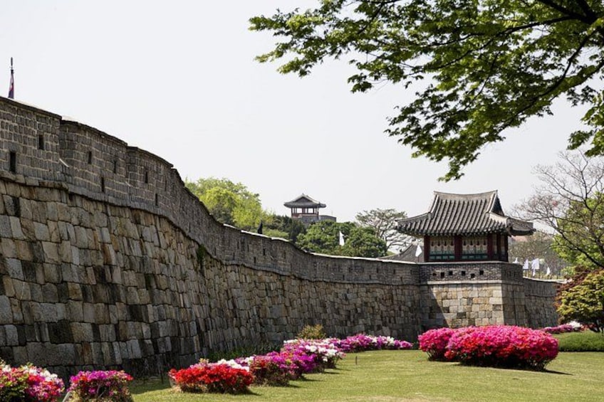 Un mur de pierre, un bâtiment de style traditionnel et des plantes en fleurs. 3