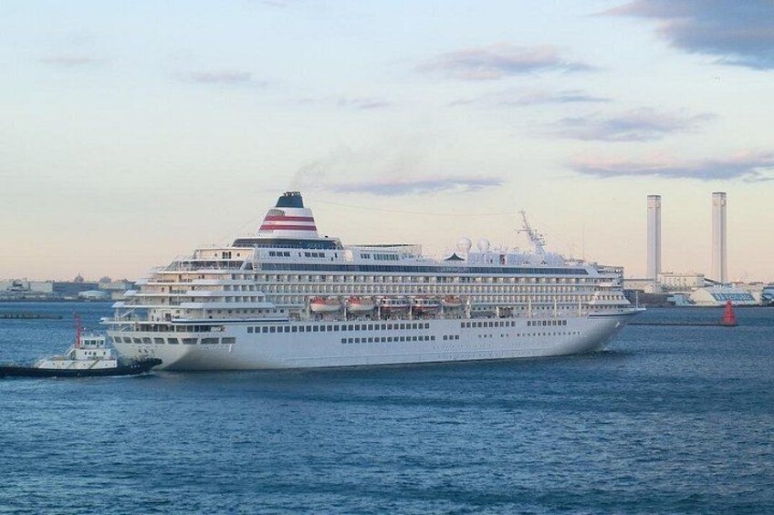 A large cruise ship with multiple decks and a smaller tugboat in the foreground. 1