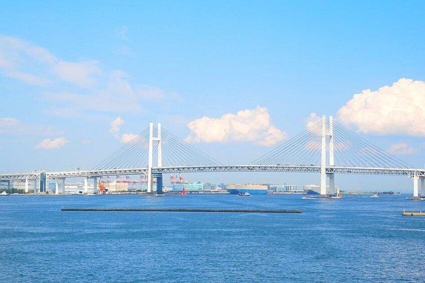 A large suspension bridge over a body of water with multiple lanes, construction cranes, and a clear sky. 2
