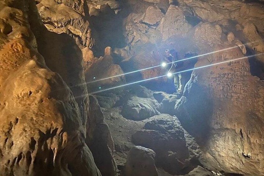 A cave with stalactites and stalagmites, a person exploring, and a flashlight illuminating the area. 1
