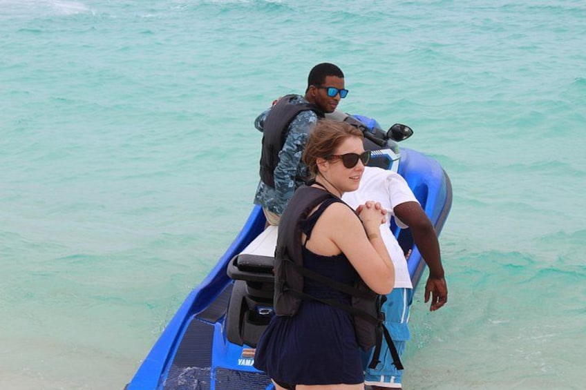 Un jet ski azul con dos personas a bordo, una usando chaleco salvavidas, y el agua es turquesa. 1