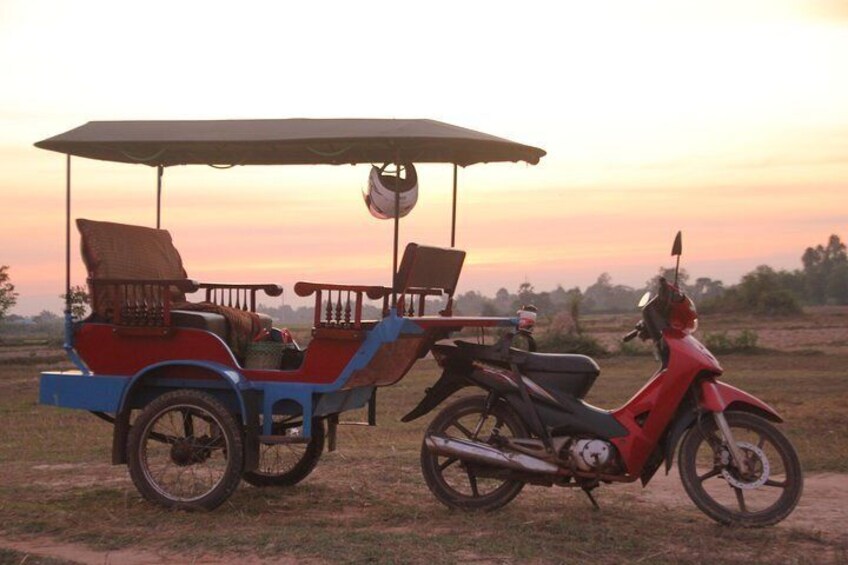 A red scooter and a blue and red rickshaw parked on a dirt road during sunset. 3