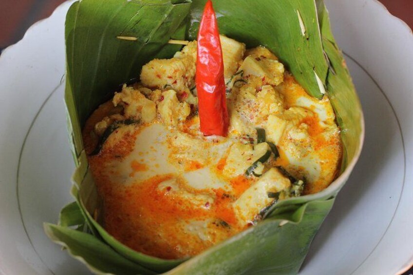 A dish of curry in a banana leaf bowl with a red chili on top. 4