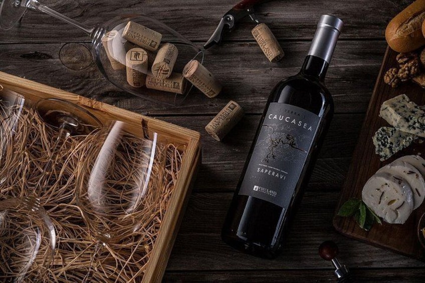 Una botella de vino Saperavi, corchos, copas y queso sobre una mesa de madera. 2